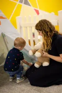 NDIS toddler boy engaging in speech therapy with a female speech pathologist holding a stuffed toy, focusing on toddler speech milestones and word count