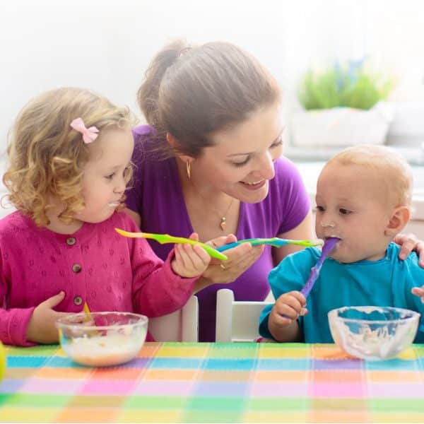 Parent feeding their child and baby with spoons