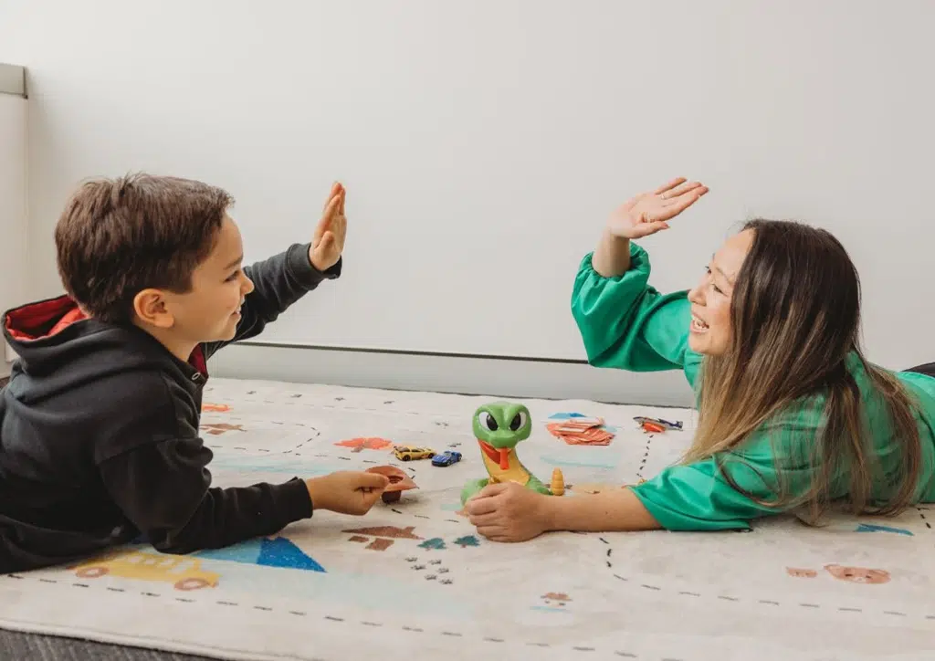 Speech pathologist giving a high five to a young boy with Global Developmental Delay during a speech therapy session.