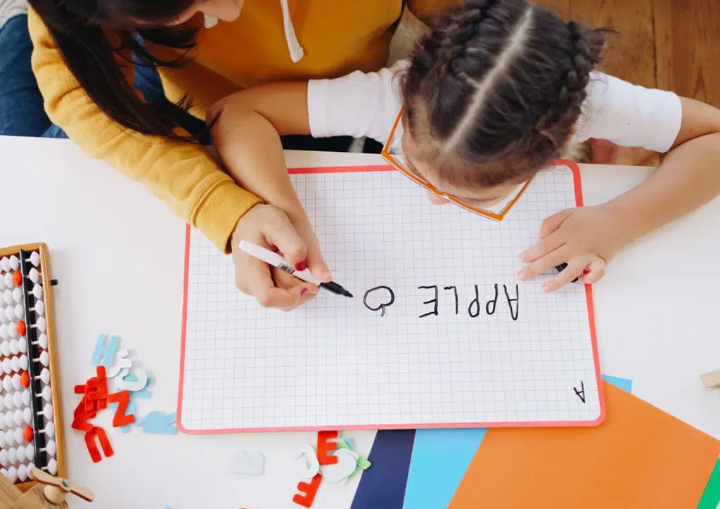 Speech pathologist guiding a young child with dysgraphia to practise writing on a whiteboard using a pen during speech therapy session