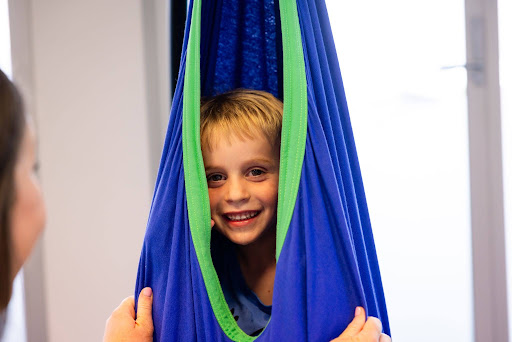 Smiling boy in a sensory swing during a fun Speech Pathology Ashfield session.