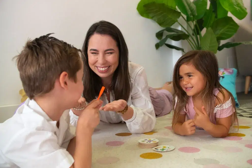 A young girl smiling and engaging in a play-based speech therapy session, used to assess and treat a articulation disorder.