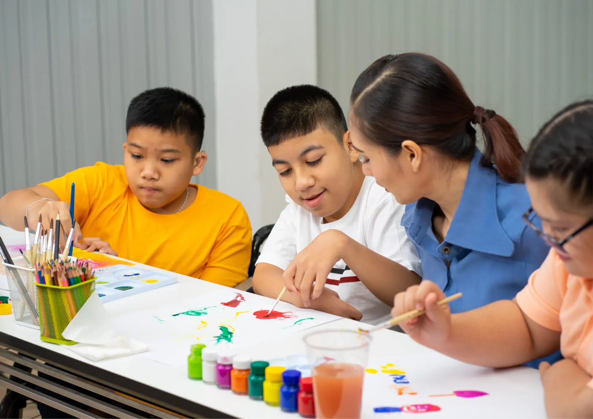 Neurodiverse affirming speech therapy session with a speech pathologist supporting three NDIS participants during a creative painting activity