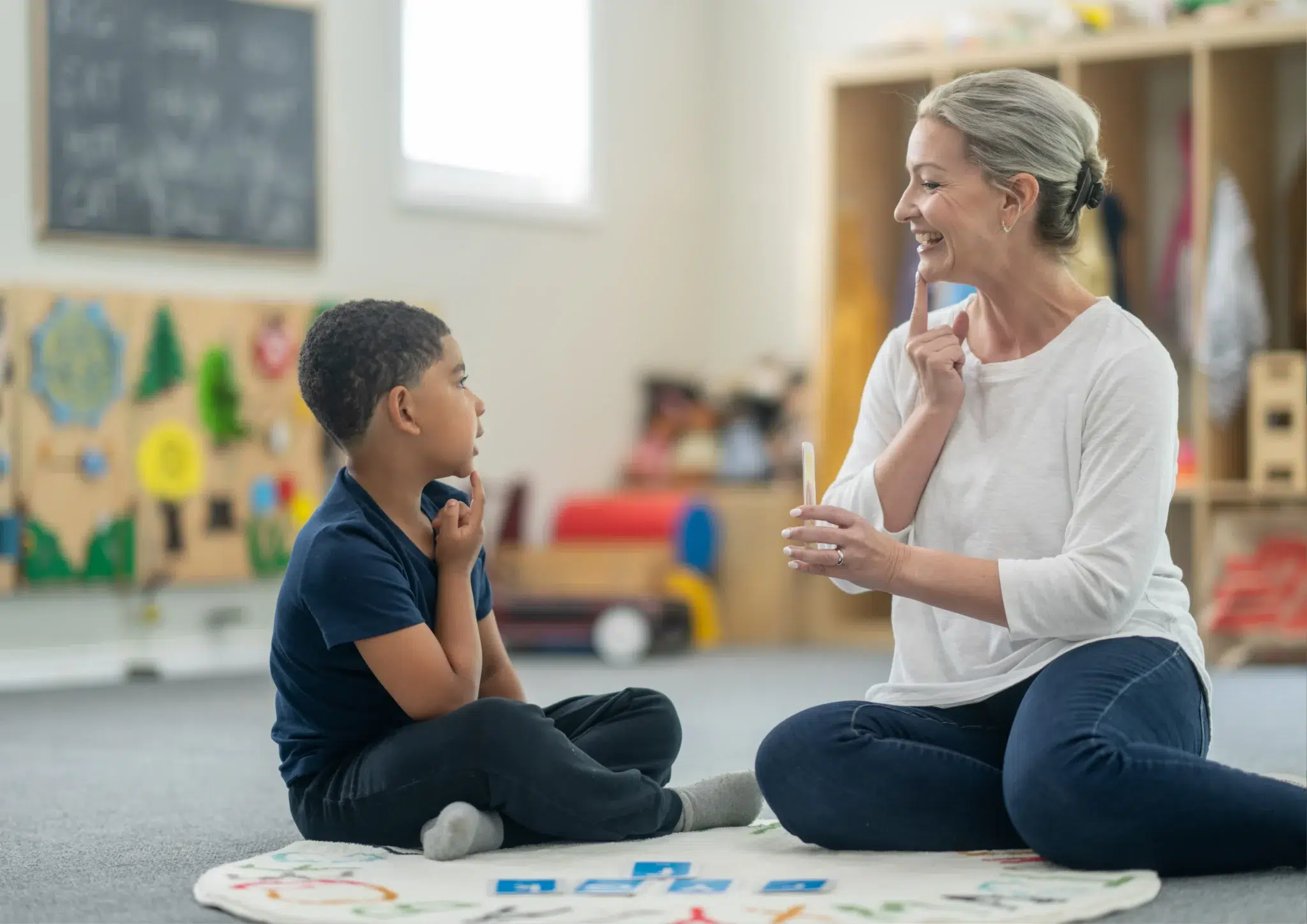 Speech pathologist sitting on the floor with a young boy during dysphonia speech therapy focused on developing communication and voice skills.