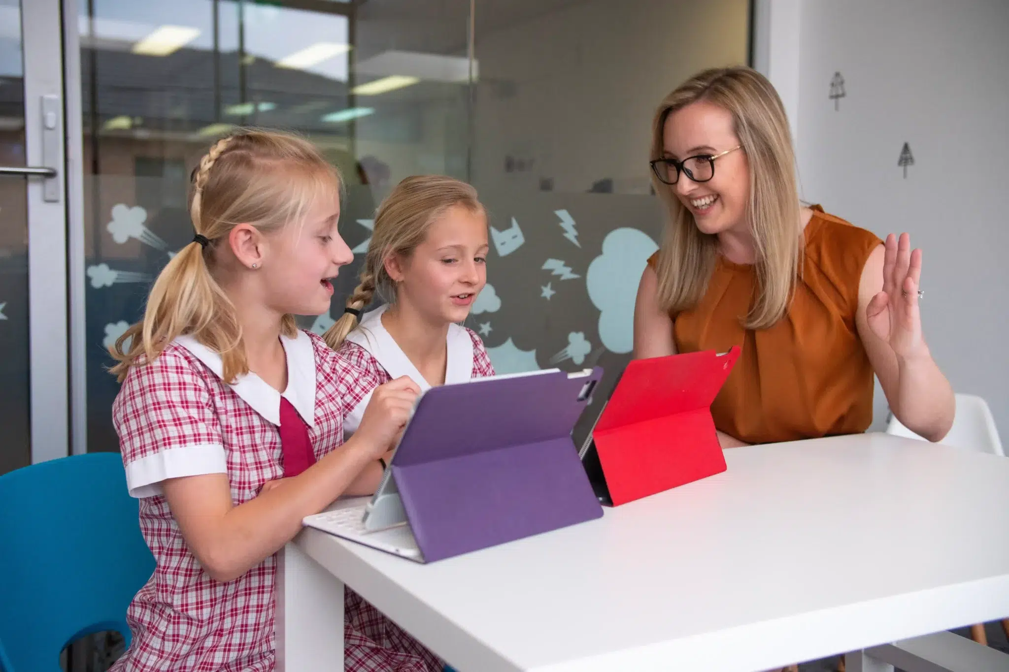 Two young girls interact with tablet communication setups during a child-led AAC speech therapy session with a female therapist.