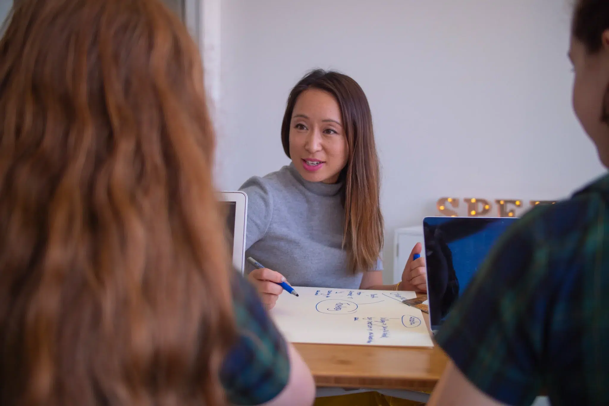A speech therapist smiling during a Lidcombe Program speech therapy session, seated at a wooden desk with diagrams and notes.
