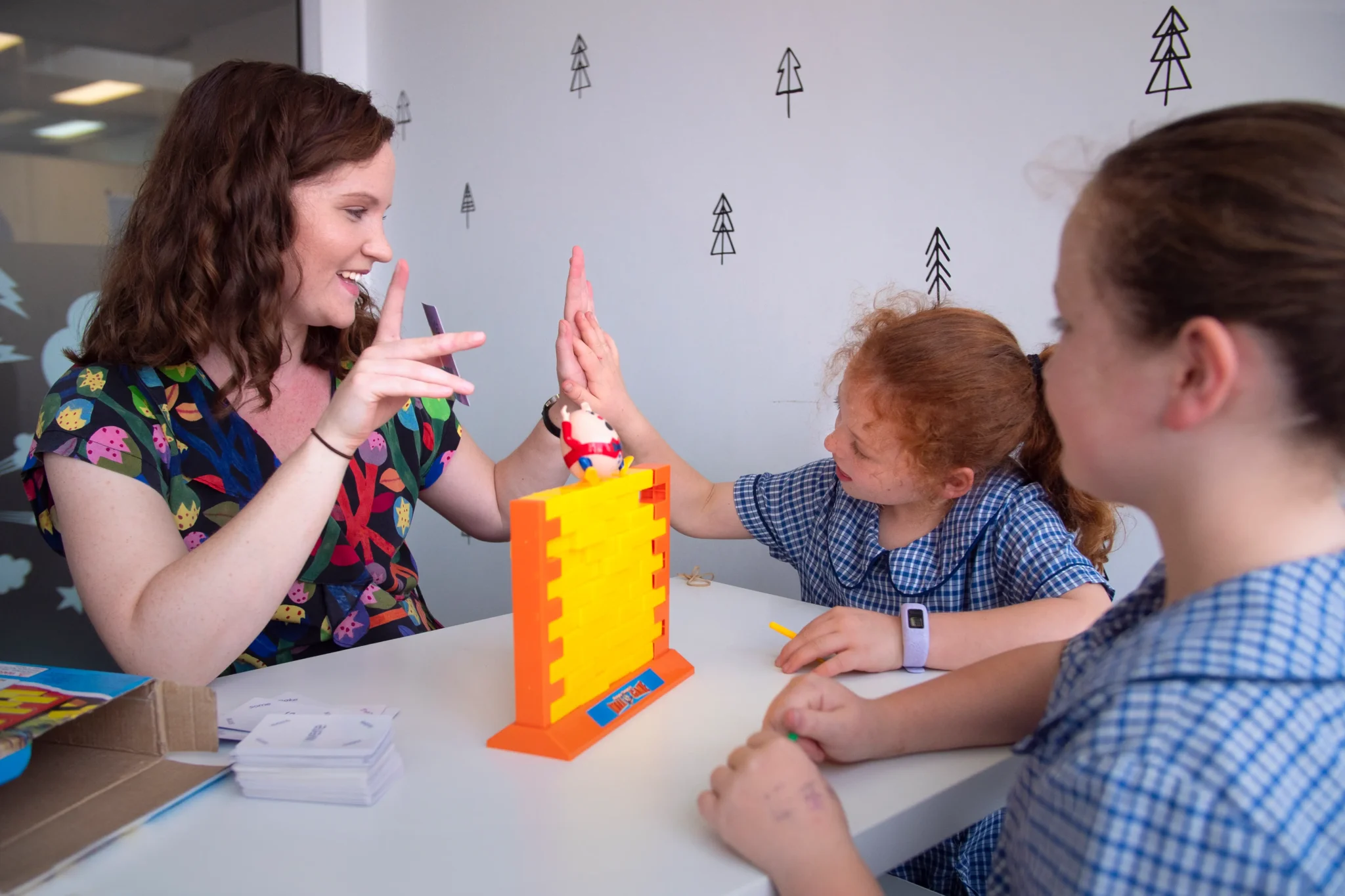 Speech pathologist using Keyword Sign and a high five to celebrate with two girls during a block wall game