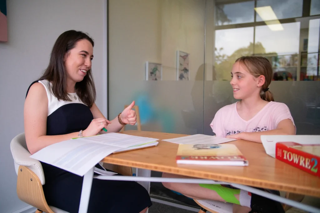 Speech pathologist using Keyword Sign and a high five to celebrate with two girls during a block wall game